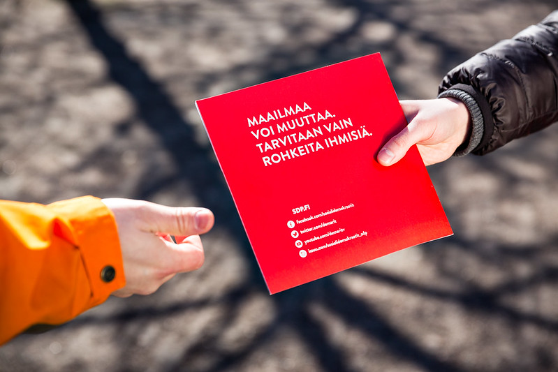 Vaaliesitteen jako kädestä käteen. Esitteessä teksti Maailmaa voi muuttaa, tarvitaan vain rohkeita ihmisiä.