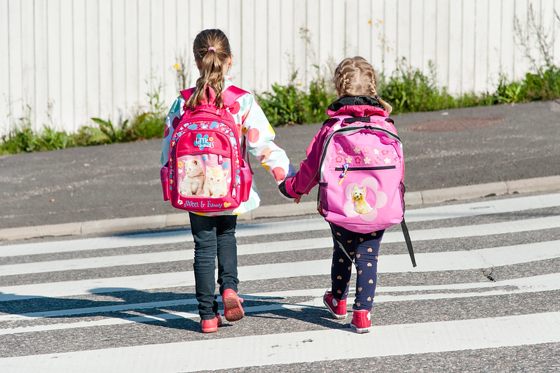 Kaksi pientä koululaista ylittämässä suojatietä reput selässään