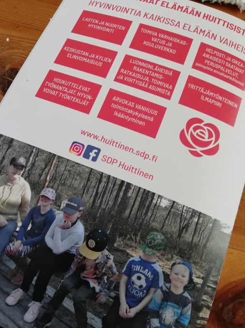 Vaaliesitteen takakansi, missä vaaliteemat ja kuvassa aikuinen ja viisi lasta penkillä pitkospuureitin varrella