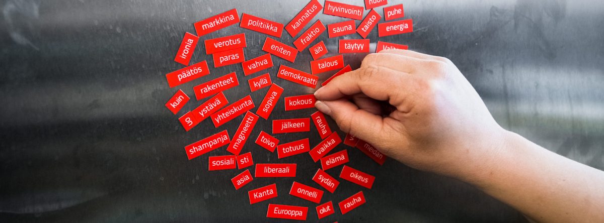 Jääkaapin ovessa punaisia magneetteja, joissa elämään liittyviä asioita ja teemoja, kuvassa myös käsi